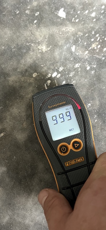 Moisture meter showing a wet reading on a concrete floor